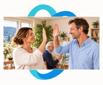Zwei pflegende Angehörige setzen zum High-Five an, während ihr Vater im Hintergrund im Sitzen malt.